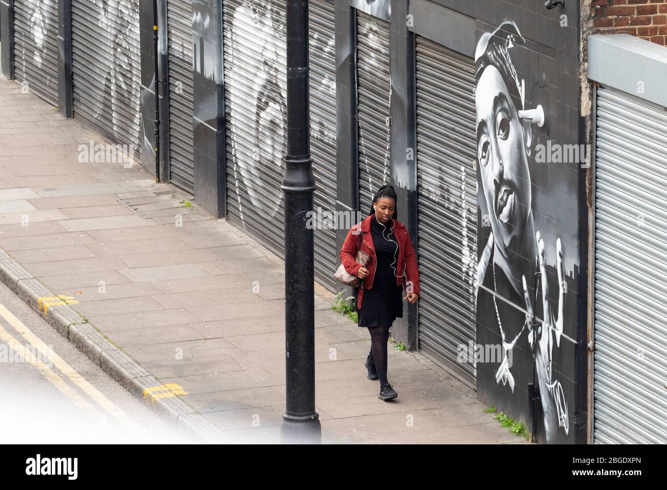 Eine Frau, die an Straßenkunst berühmter Rapper auf der Atlantic Road, Brixton, London vorbeigeht Stockfoto