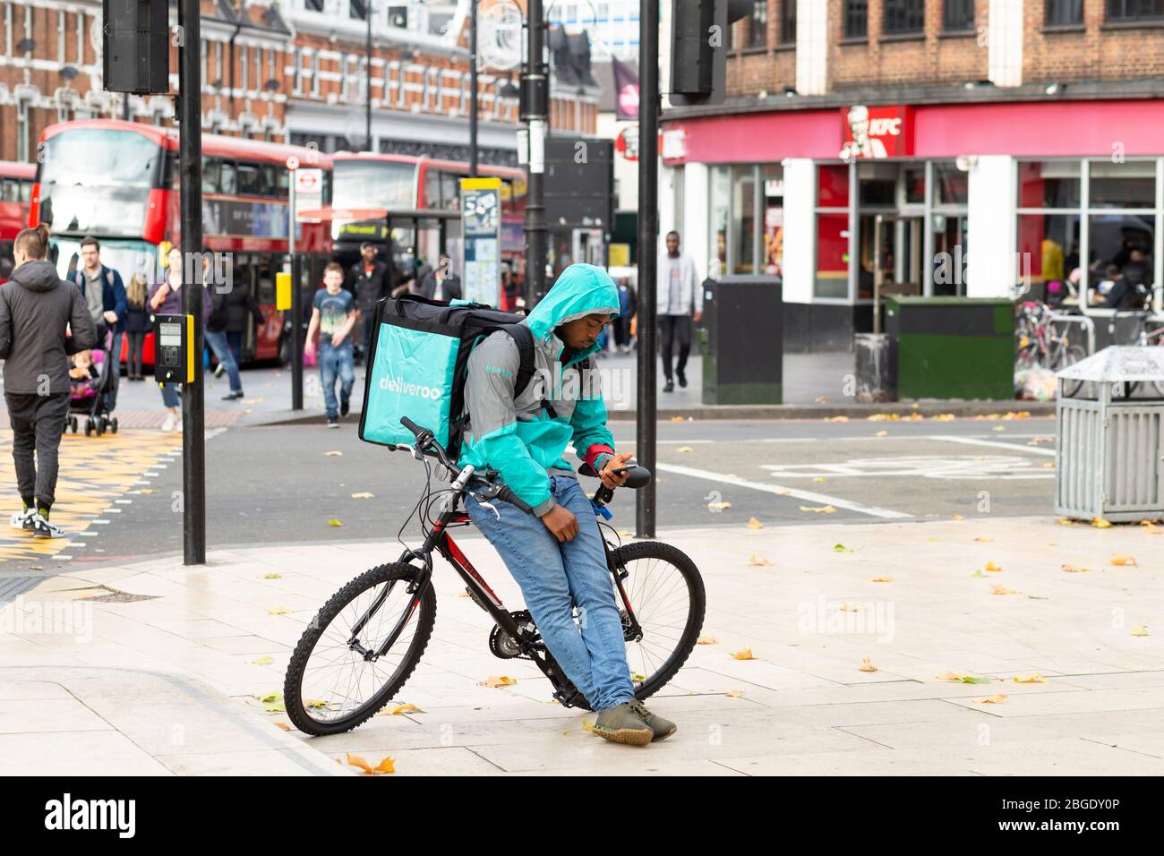 Ein deliveroo-Fahrer, der sich auf sein Fahrrad stützt und sein Telefon in Windrush Square, Brixton, London, überprüft Stockfoto