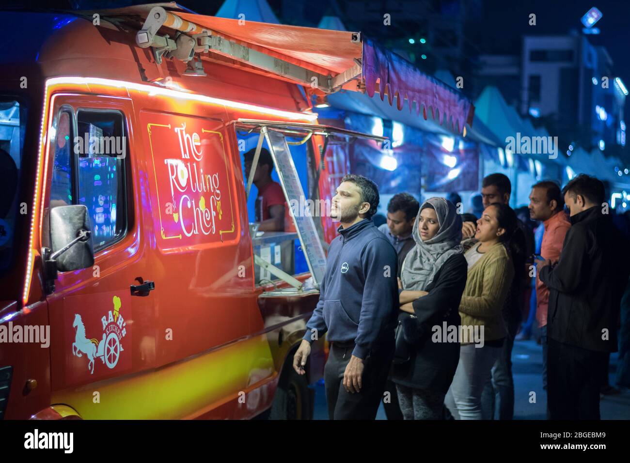 Eine Gruppe von Menschen, die nachts vor einem roten Food Truck auf ihre Bestellungen warten Stockfoto