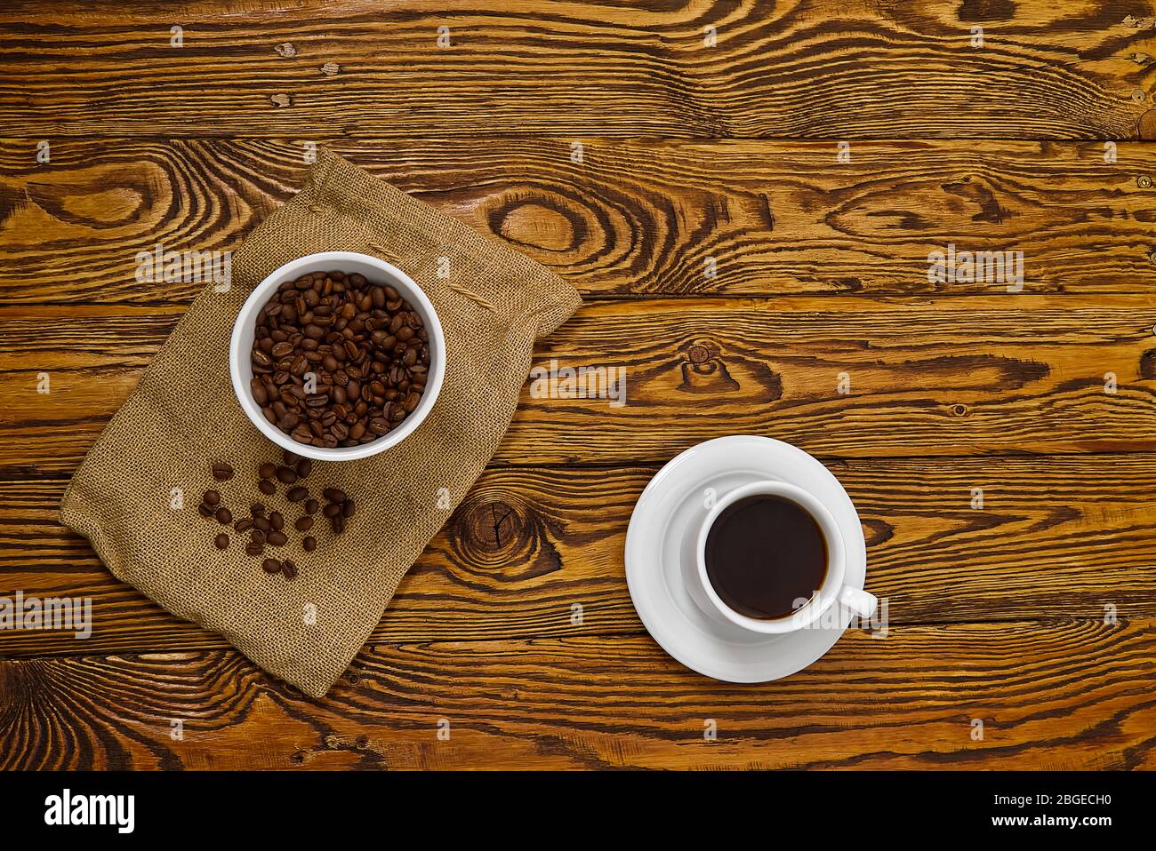 Weiße Kaffeetasse mit aromatischem Kaffeegetränk auf braunem Holztisch. Kaffeesamen auf antikem Holztisch mit Tasse Kaffee Getränk. Stockfoto