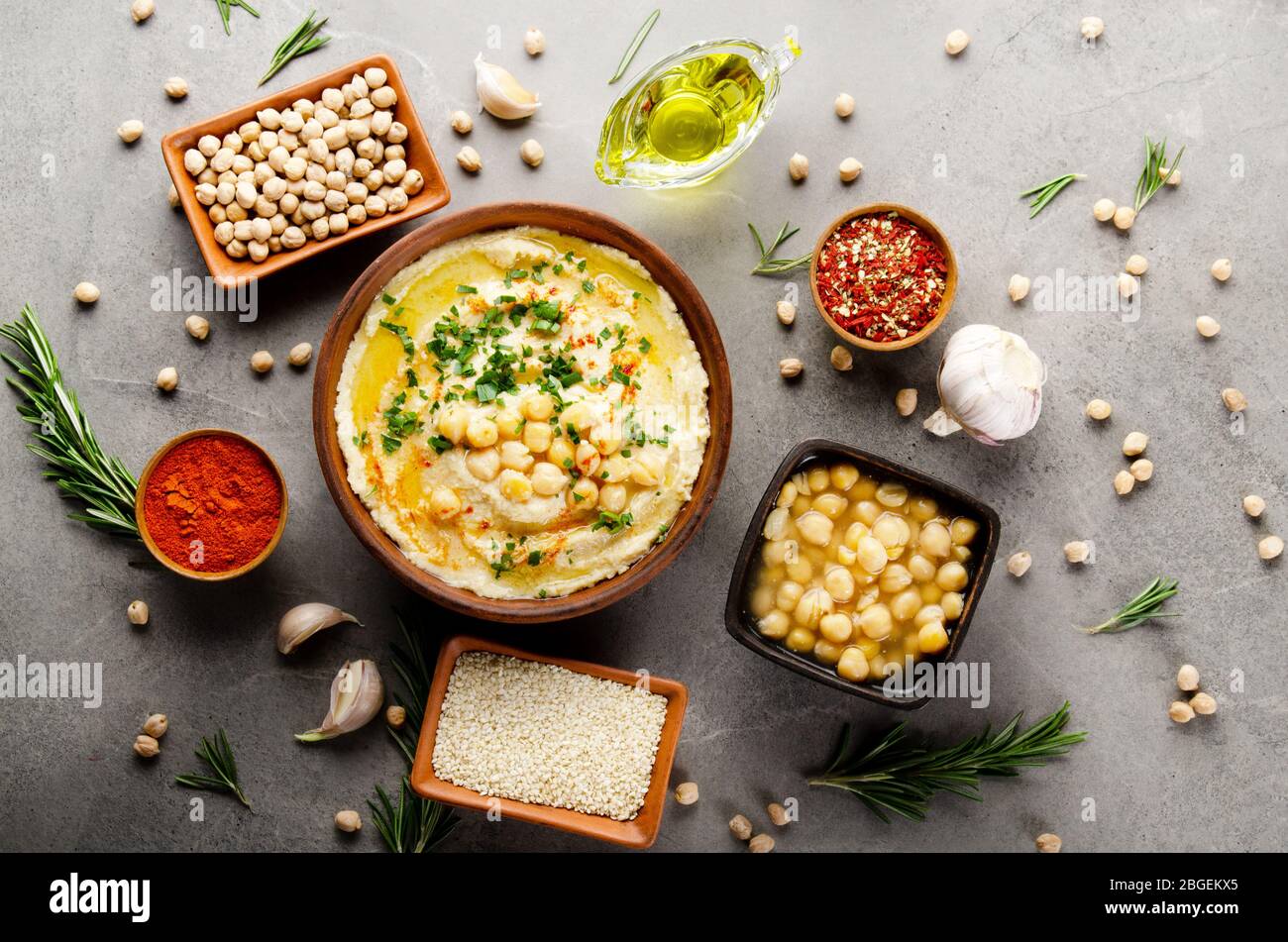 Hummus mit Kichererbsen, Olivenöl und grünen Korianderblättern auf Steintisch mit verschiedenen Gewürzen beiseite. Flaches Lay Stockfoto