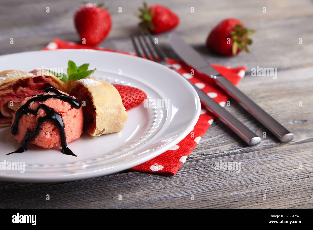 Leckerer selbstgemachter Strudel mit Eis, frischen Erdbeer- und Minzblättern auf Teller, auf Holzhintergrund Stockfoto