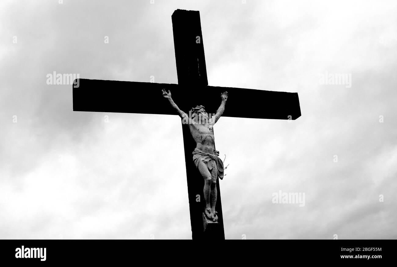 Kruzifix mit vergoldeter Skulptur Jesu auf Holzkreuz gegen dunklen Himmel. Stockfoto