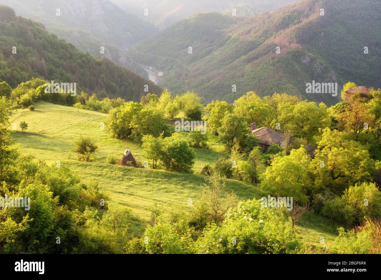 Der Frühling kommt... Erstaunliche Frühling Blick mit einem kleinen Dorf in Rhodopi Gebirge, Bulgarien. Herrliche Landschaft, grüne Felder, kleine Häuser. Stockfoto