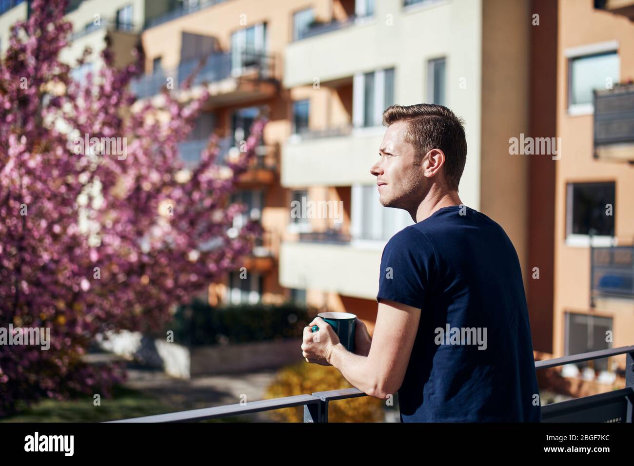 Frühlingsmorgen zu Hause. Junger Mann mit Tasse Tee oder Kaffee auf dem Balkon. Stockfoto