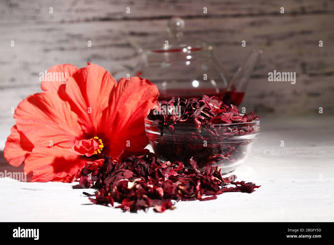 Hibiscus Tee in Glas Teekanne und Blume auf Farbe Serviette auf Holzhintergrund Stockfoto