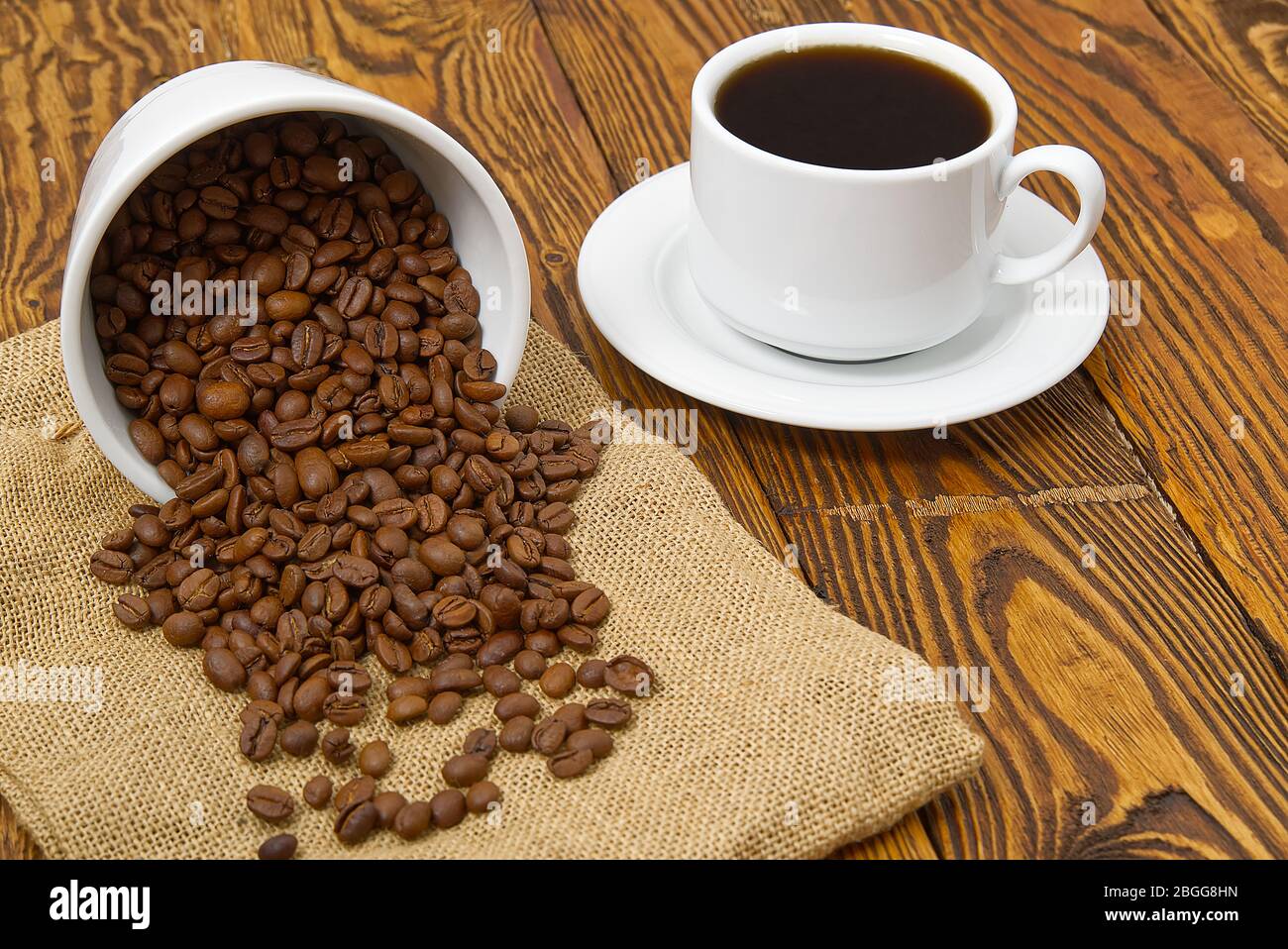 Weiße Kaffeetasse mit aromatischem Kaffeegetränk auf braunem Holztisch. Kaffeesamen auf antikem Holztisch mit Tasse Kaffee Getränk. Stockfoto