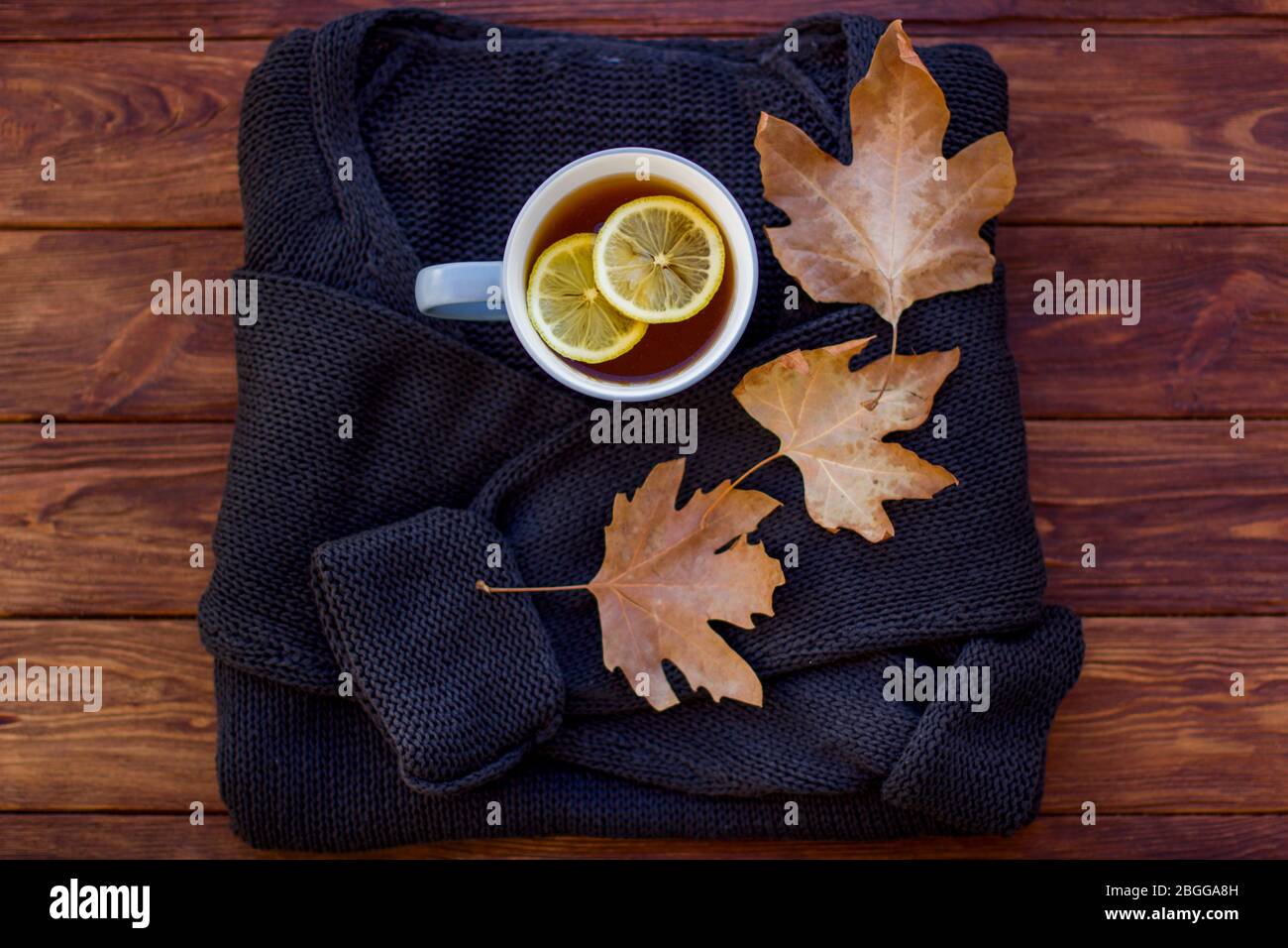 Herbstgestaltung mit heißem Tee mit Zitrone auf einem Pullover und trockenen Blättern. Brauner Hintergrund. Stockfoto