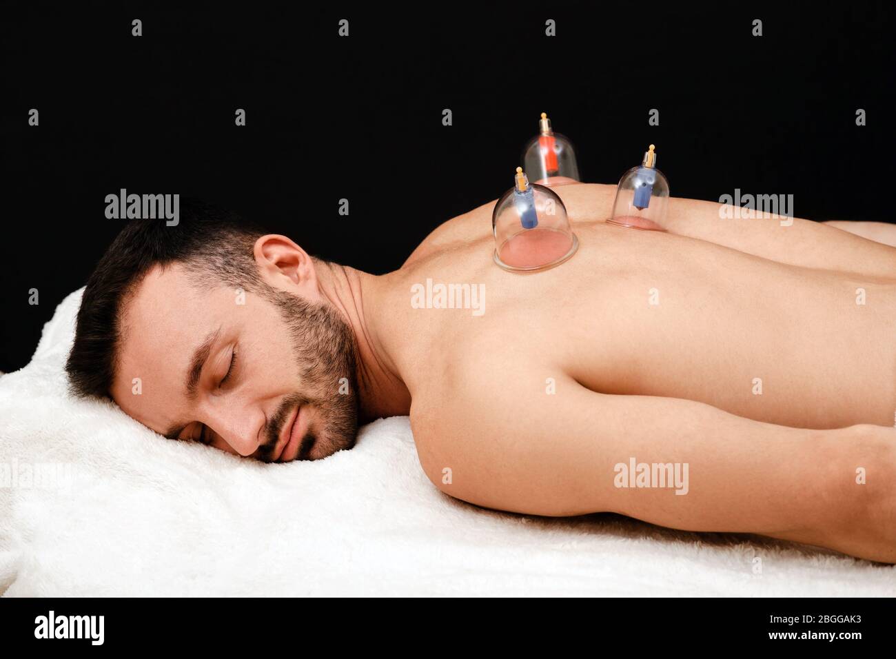 Der Mann entspannt sich im Spa mit Vakuumbechern auf dem Rücken. Vakuumsauger für die Gesundheitsbehandlung Nahaufnahme auf schwarzem Hintergrund Stockfoto