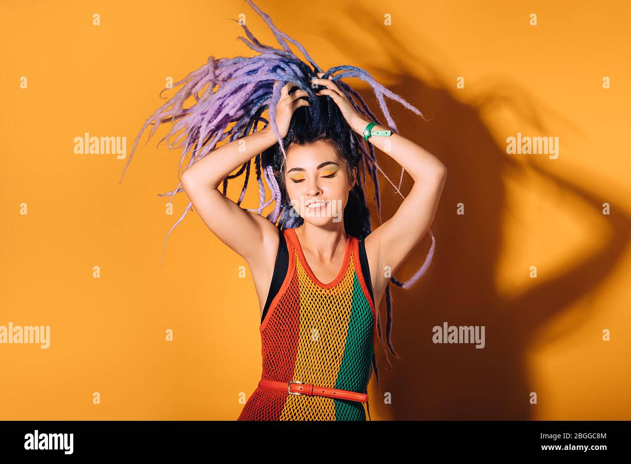 Hipster Frau im Rasta-Kleid und einem Rasta-Color Make-up tanzt zu Reggae-Musik. Orangefarbener Hintergrund Stockfoto