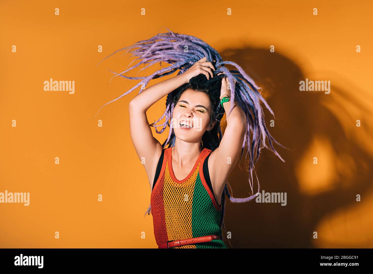 Frau mit lila Dreadlocks tanzt auf einem orangefarbenen Hintergrund. Hipster Frau genießt das Leben. Stockfoto