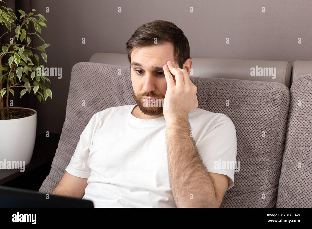 Stress kaukasischen düsteren Mann im Stress arbeitet aus dem Home Office mit Laptop und Internet. Telearbeit, Freiberufler, Arbeitsplatz im Home Office auf dem Sofa Stockfoto