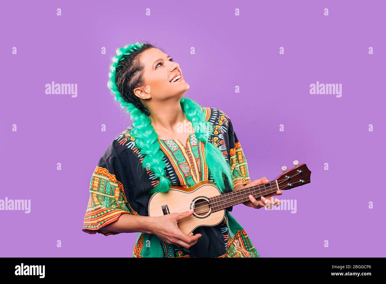 Schöne Frau mit Kanekalon Zöpfe spielen Ukulele. Stilvolle Frisur Kanekalon Zöpfe. Hawaiianische Gitarre auf violettem Hintergrund Stockfoto