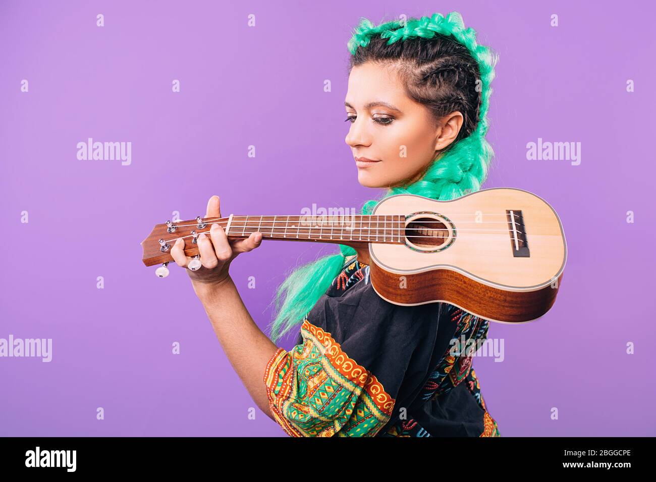 Rastafari Frau mit Ukulele auf der Schulter. Musikinstrument Ukulele. Hawaiianische Gitarre auf violettem Hintergrund Stockfoto