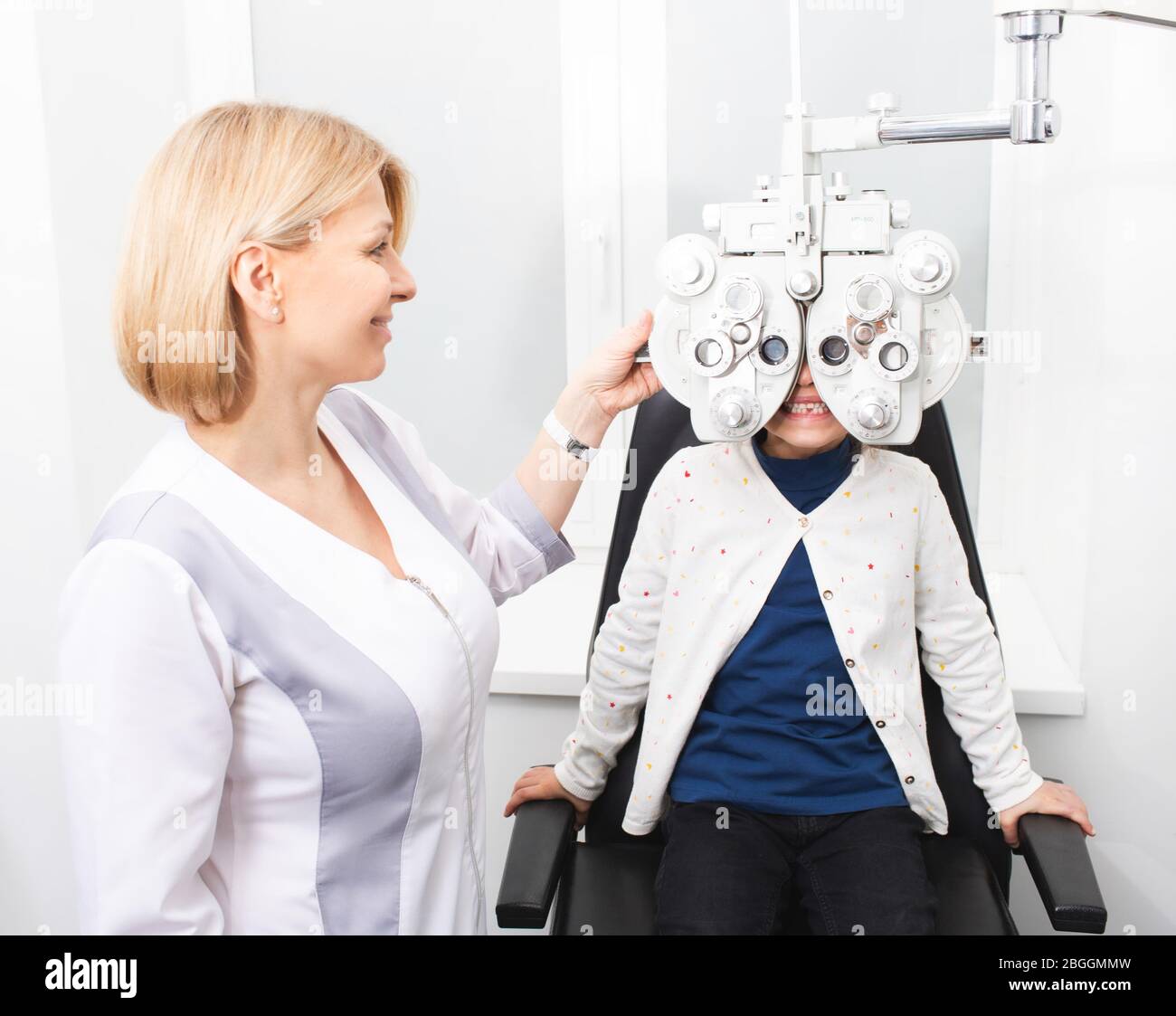 Frau Optometristin überprüft die Vision eines jungen Mädchens. Mädchen lächelt und hat keine Angst, ihr Augenlicht in der Klinik zu überprüfen. Sehbehinderung bei Kindern Stockfoto