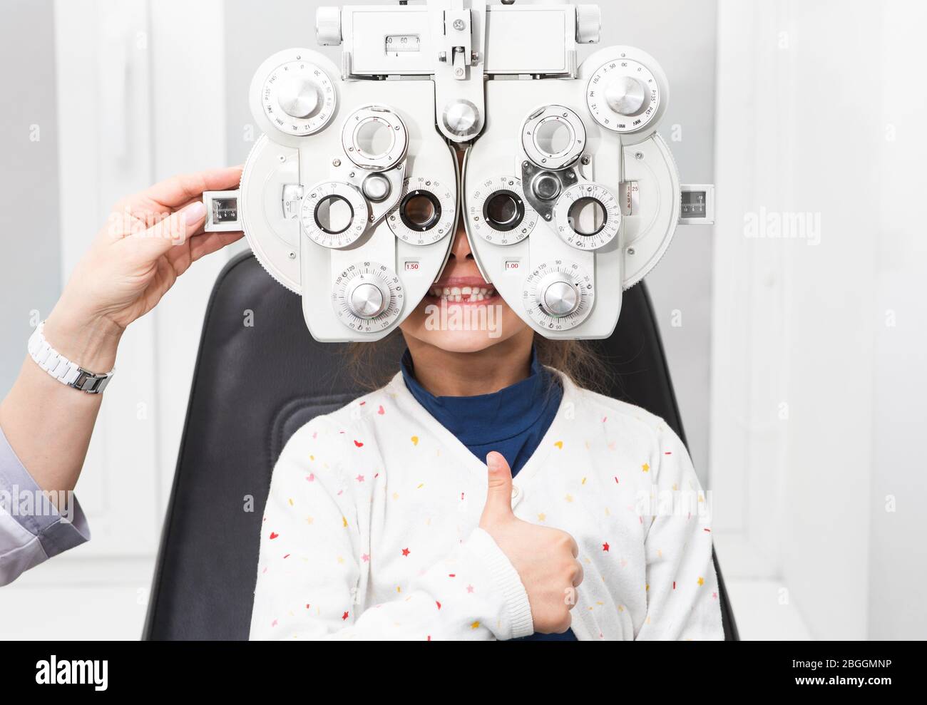 Mädchen zeigt Daumen nach oben bei einem Augenarzt Termin. Foropter - ein  Gerät zur Messung von Brechungsfehlern und zur Bestimmung von Informationen  für eine Präs Stockfotografie - Alamy