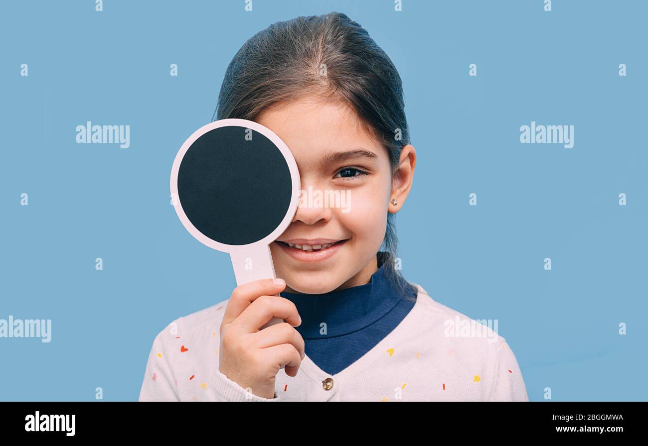Lächelndes Mädchen, das die Augen überprüft und die Augen mit einem speziellen Werkzeug auf blauem Hintergrund schließt. Vision Test Konzept Stockfoto