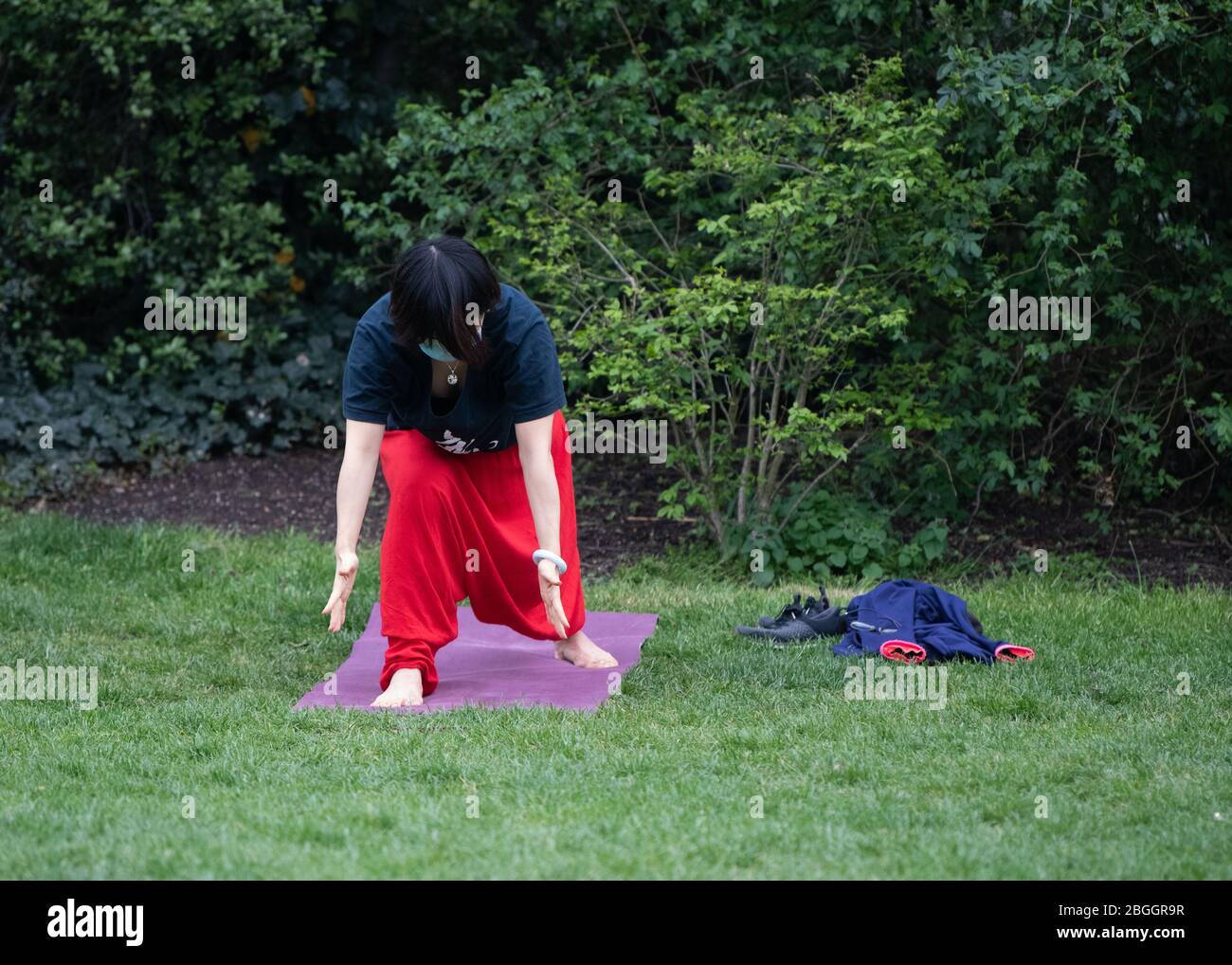 Frau mit Gesichtsmarkierung beim Yoga-Training im Kensington Park während der Sperrung, wenn nur eine Übung im Freien erlaubt ist. London, Großbritannien Stockfoto