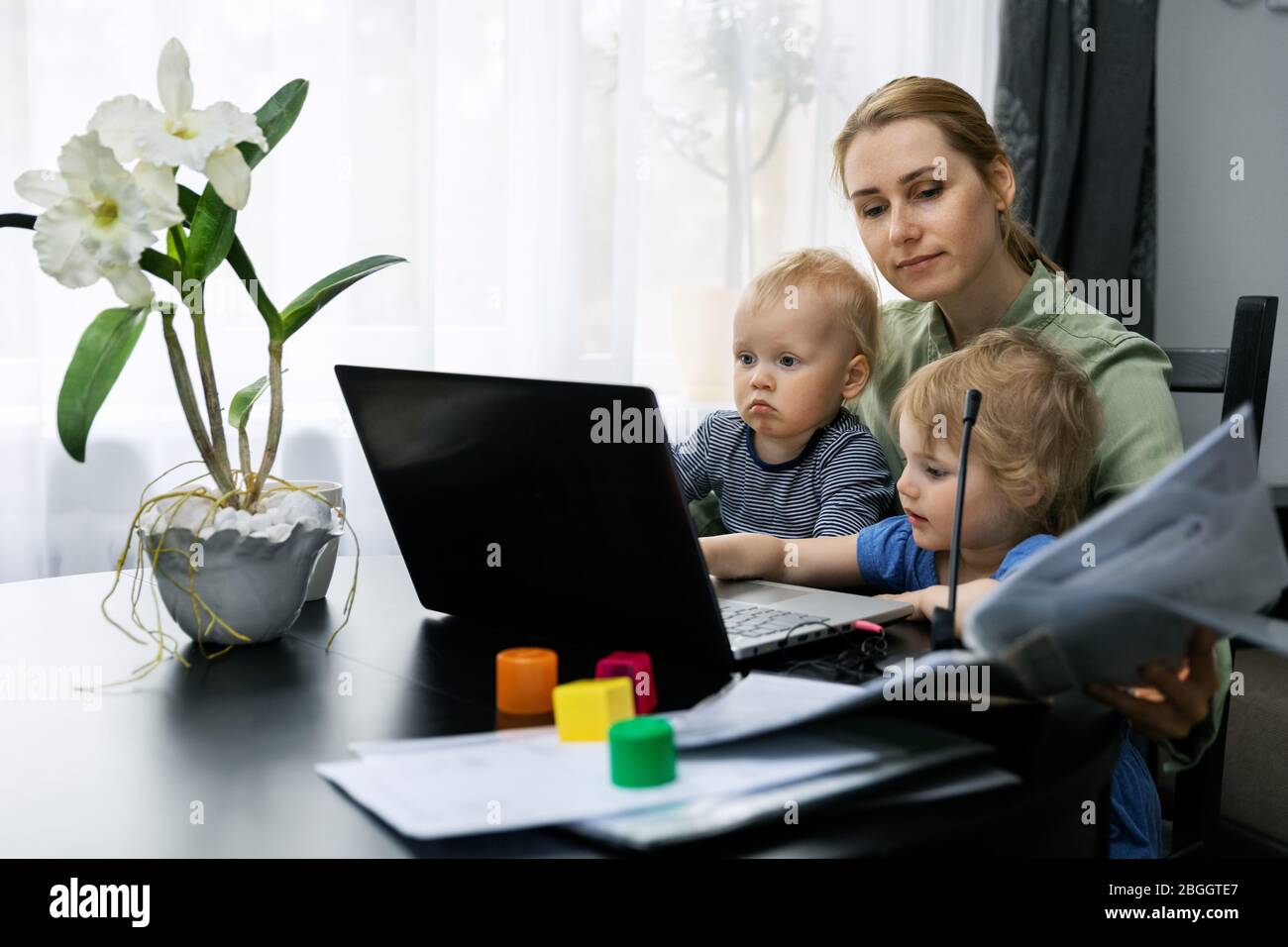 Mutter arbeitet von zu Hause. Mit Laptop am Schreibtisch mit Kindern auf ihrem Schoß Stockfoto