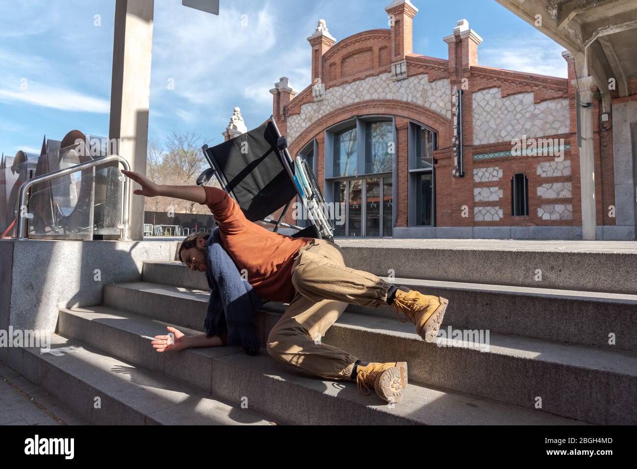 Behinderter Latino-junger Mann im Rollstuhl fällt eine Treppe hinunter, die er nicht mit dem Stuhl auf der Straße hinuntergehen kann Stockfoto