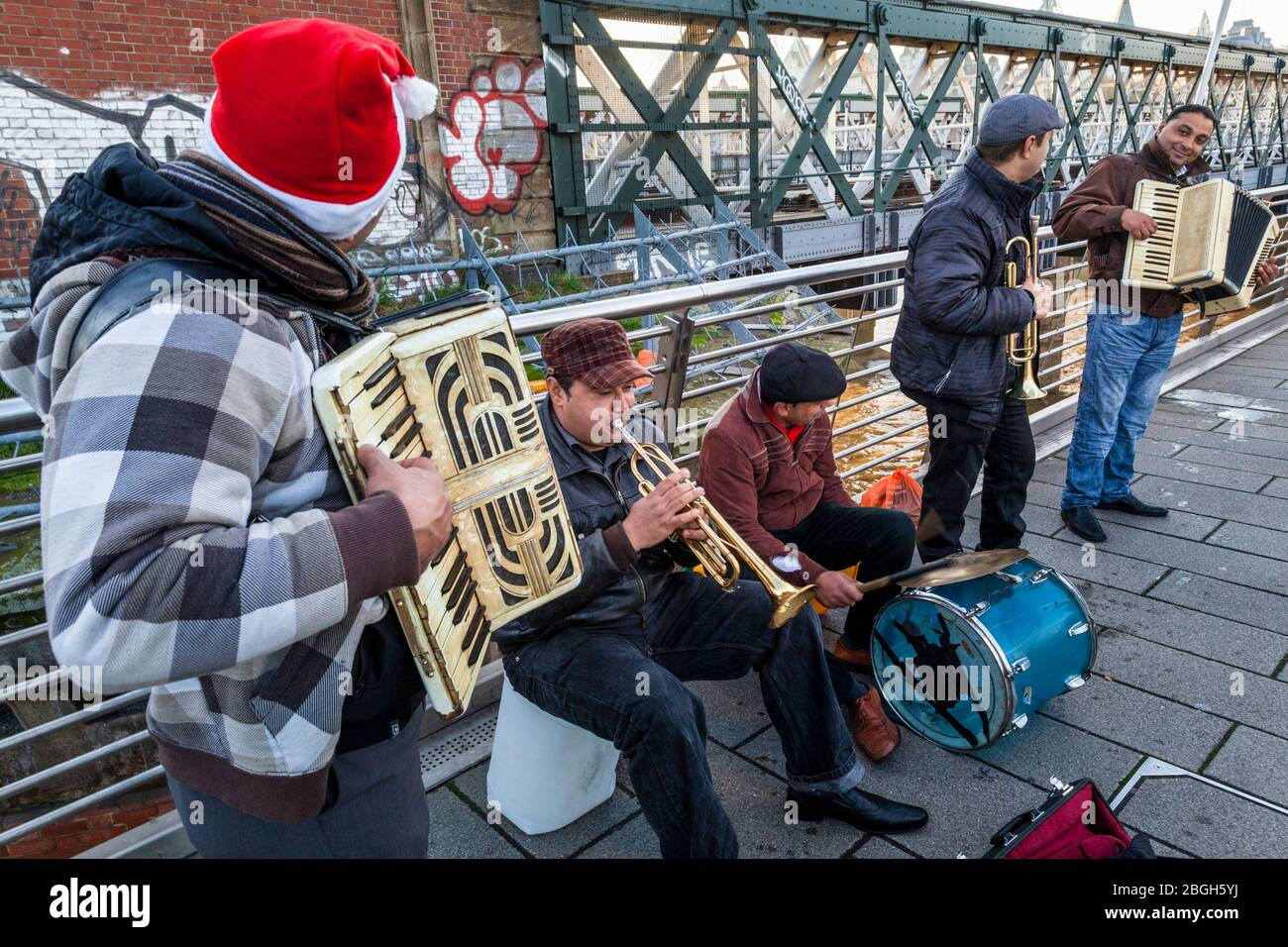 Gruppe von Musikern, die draußen buschieren. Busker spielen Musik auf Akkordeons, Trompeten und einer Trommel auf einer Brücke, London, England, Großbritannien Stockfoto