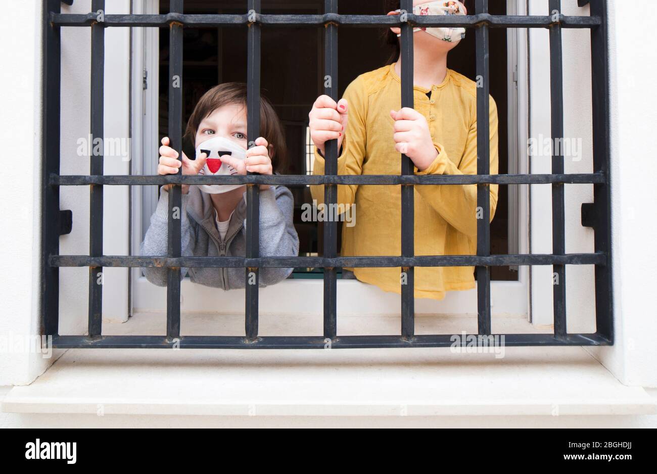 Zwei eingesperrten Kinder bleiben hinter dem Fenster der Hausbars. Der Junge schaut anklagend zur Kamera Stockfoto