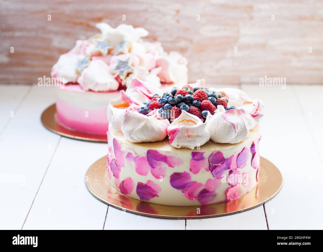 Weißer und rosa Birhday Kuchen mit Baiser und frischen Beeren, Himbeeren, Erdbeeren und Heidelbeeren. Weißer Holzhintergrund. Stockfoto