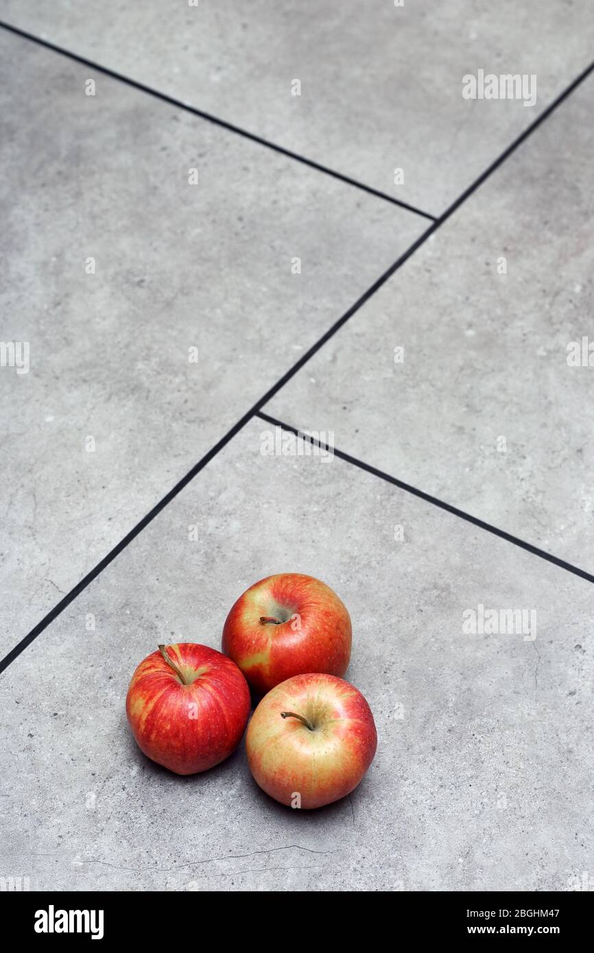 Rote Äpfel, auf grauen Bodenfliesen mit schwarzen Nähten Stockfoto