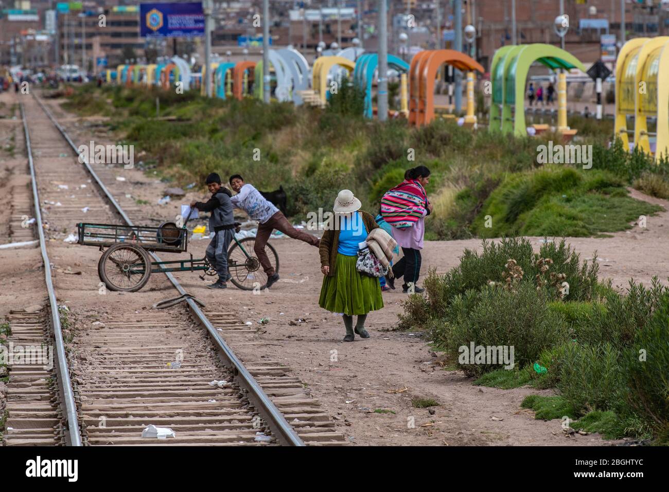 Lokale Menschen gehen über ihre täglichen Geschäfte und überqueren die Bahngleise wie der Zug von Puno nach Cusco passiert Durch Stockfoto