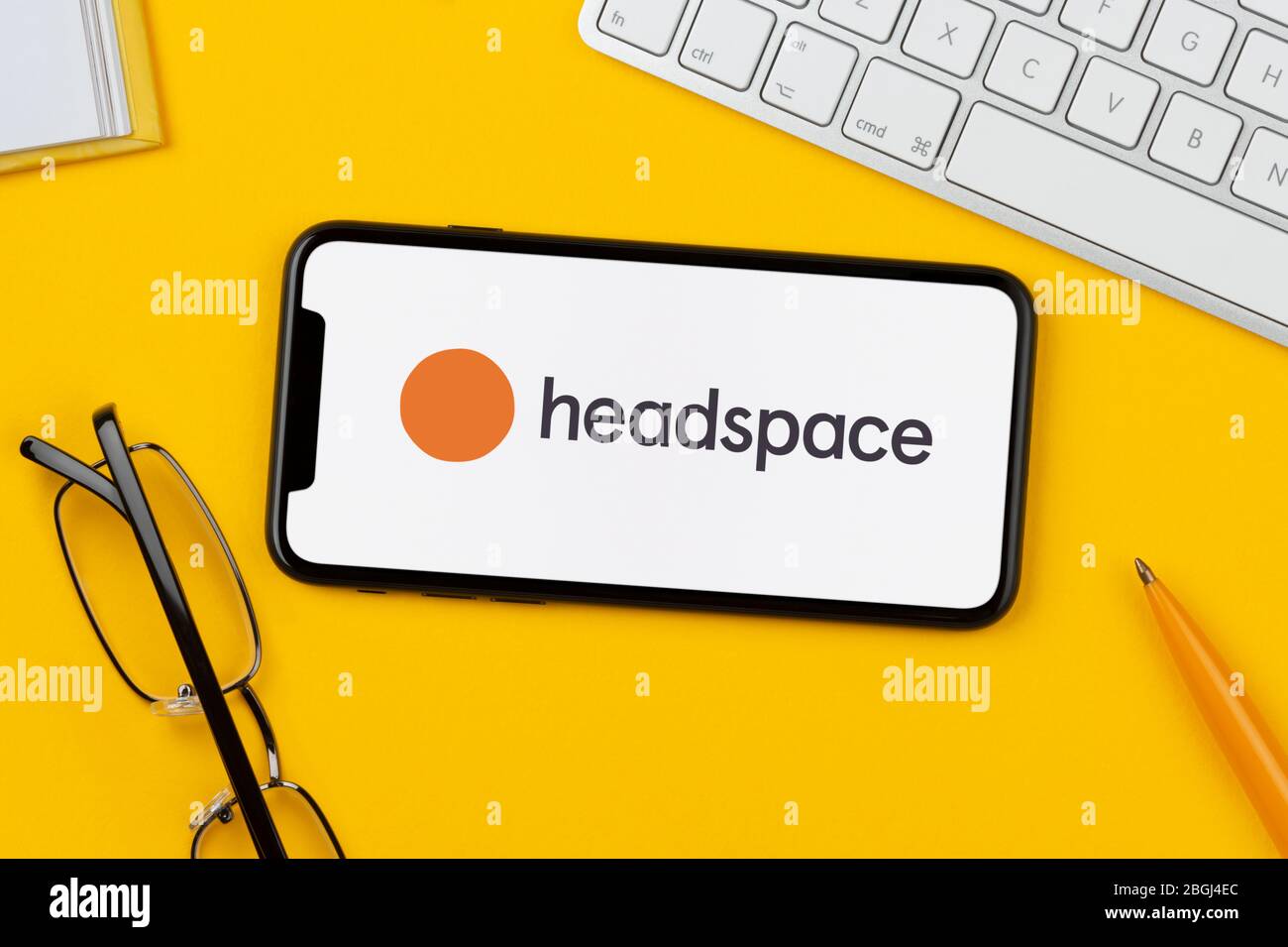 Ein Smartphone mit dem Headspace-App-Logo liegt auf einem gelben Hintergrund zusammen mit Tastatur, Brille, Stift und Buch (nur redaktionelle Verwendung). Stockfoto