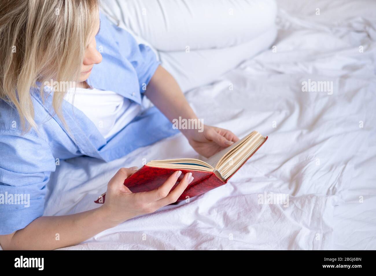 Cropped blonde Frau mit Smartphone sitzt auf dem Bett. Lesen von Nachrichten und Online-Büchern. Soziale Medien, instagram, zu Hause bleiben und Quarantäne Stockfoto