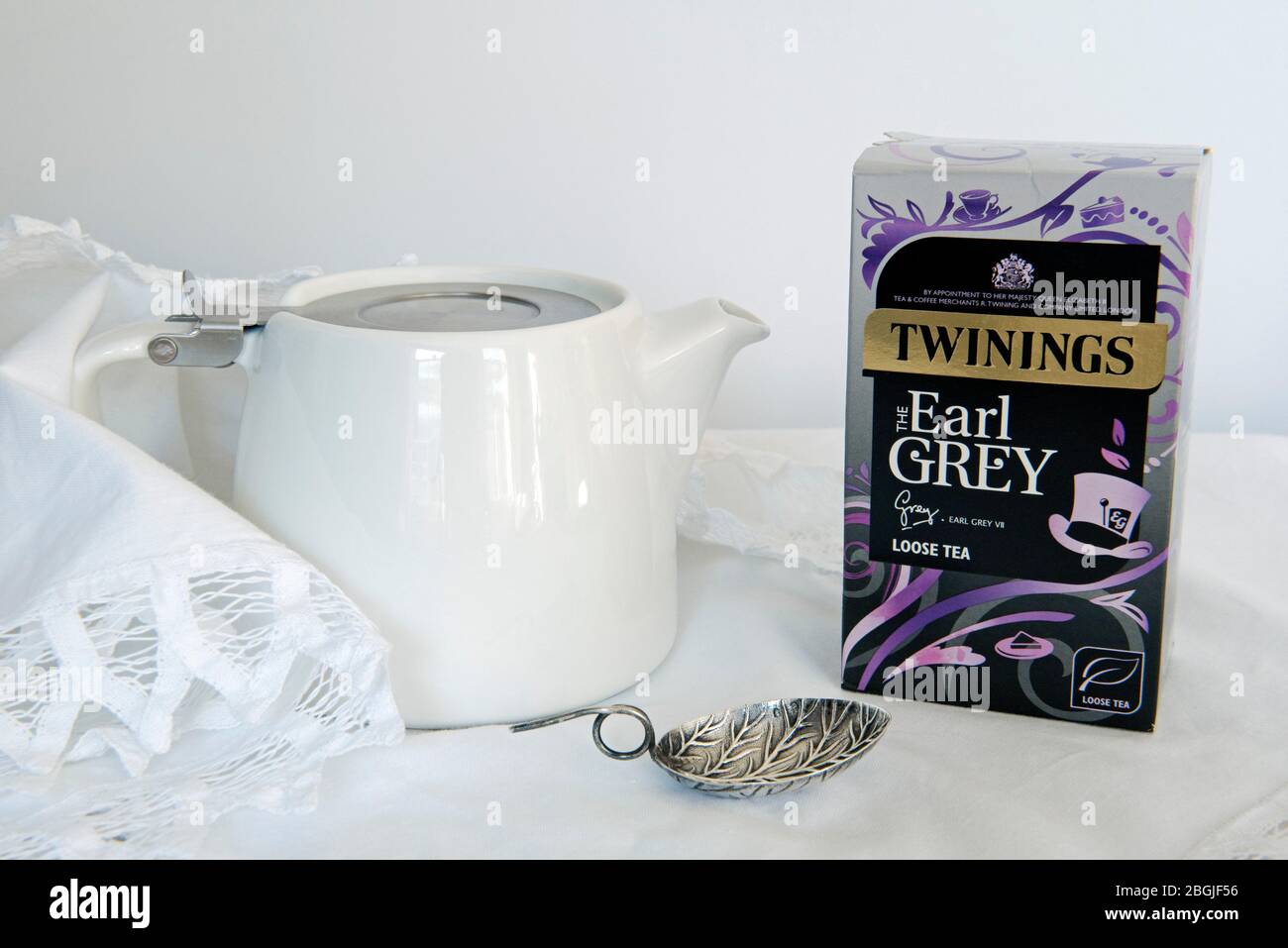 Twining's Earl Grey loser Tee im Paket mit weißer Teekanne und Teeblätterlöffel auf weißer Spitzenserviette Stockfoto