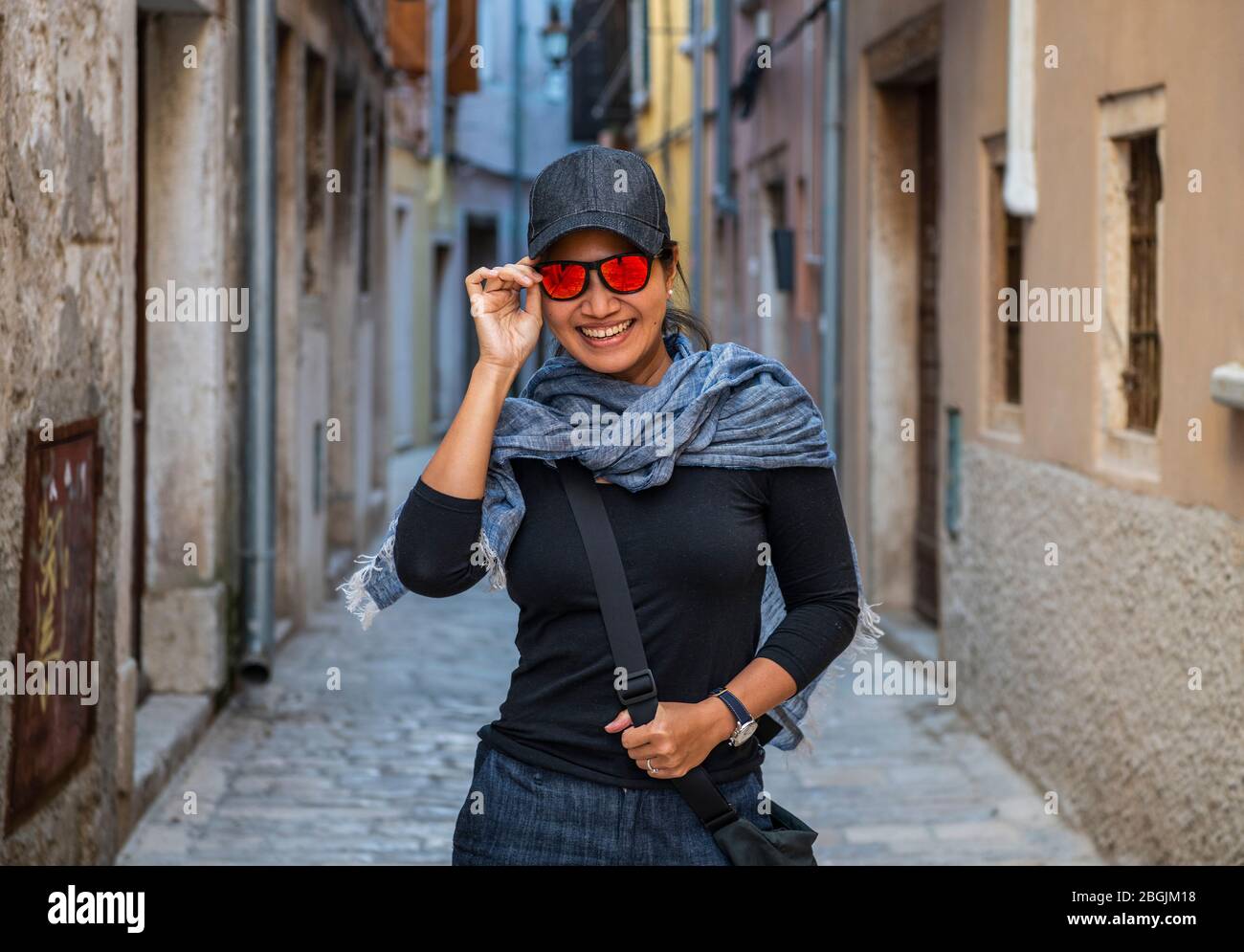 Frau, die Baseballmütze und orangefarbene Sonnenbrille in der Straßengasse trägt Stockfoto