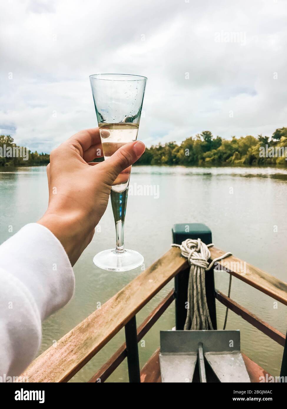 Ein Glas Champagner in der Hand auf dem Bug eines Schiffes Stockfoto
