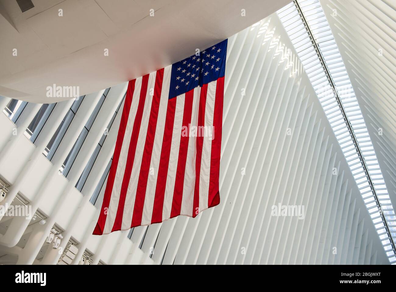 Abstract des Oculus Interior im Freedom Tower in New York City mit amerikanischer Flagge im Vordergrund und weißen vertikalen Linien. Stockfoto
