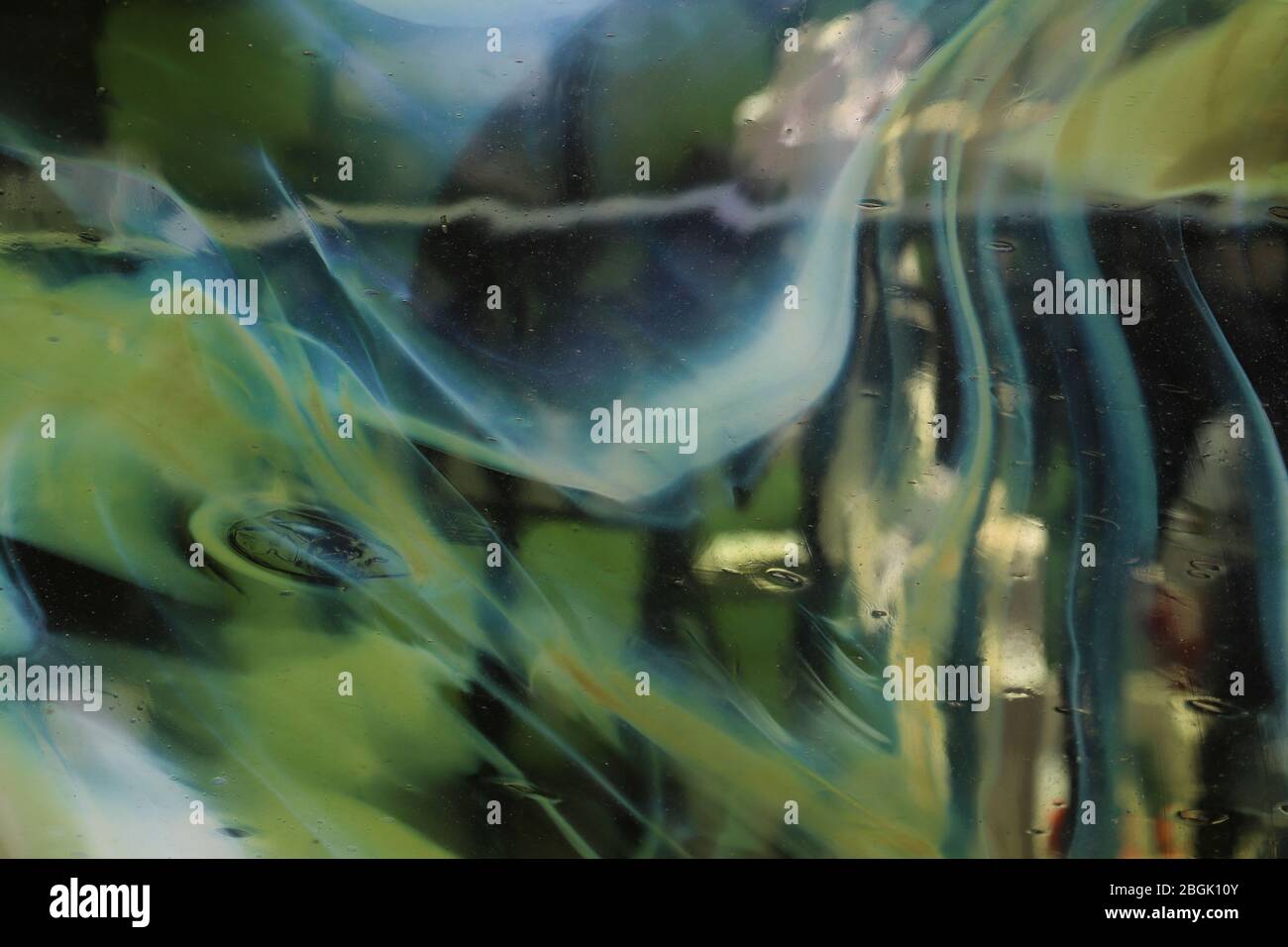 Blick durch eine Glasscheibe mit fließenden, gemischten Farben aus Weiß, Blau und Grün, die den Blick außerhalb eines Handlaufs verzerrt. Abstrakt surreal. Stockfoto