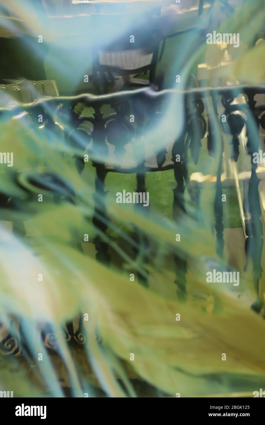 Blick durch eine Glasscheibe mit fließenden, gemischten Farben aus Weiß, Blau und Grün, die den Blick außerhalb eines Handlaufs verzerrt. Abstrakt surreal. Stockfoto