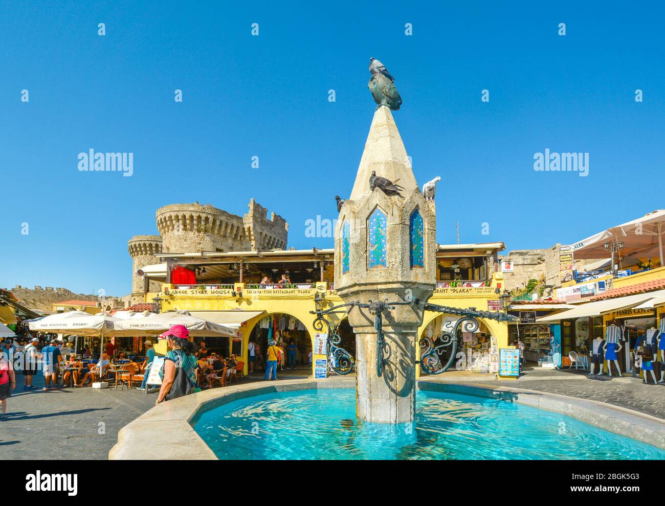 Der Brunnen bei Hippokrates Platz in der Altstadt von Rhodos Griechenland mit einer Taube saß oben auf der Eule als Touristen, Shop und im Hintergrund Essen Stockfoto