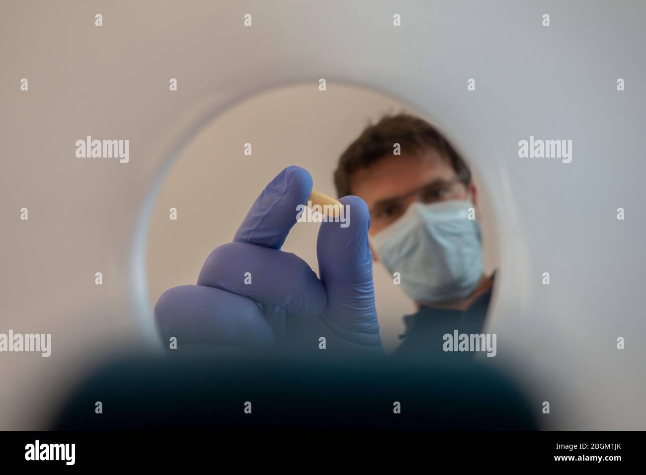 Krankenschwester mit Maske und Handschuhen legt die Therapie in Tablettenform in den Therapiebecher. Blick aus dem Inneren des Plastikbechers. Stockfoto