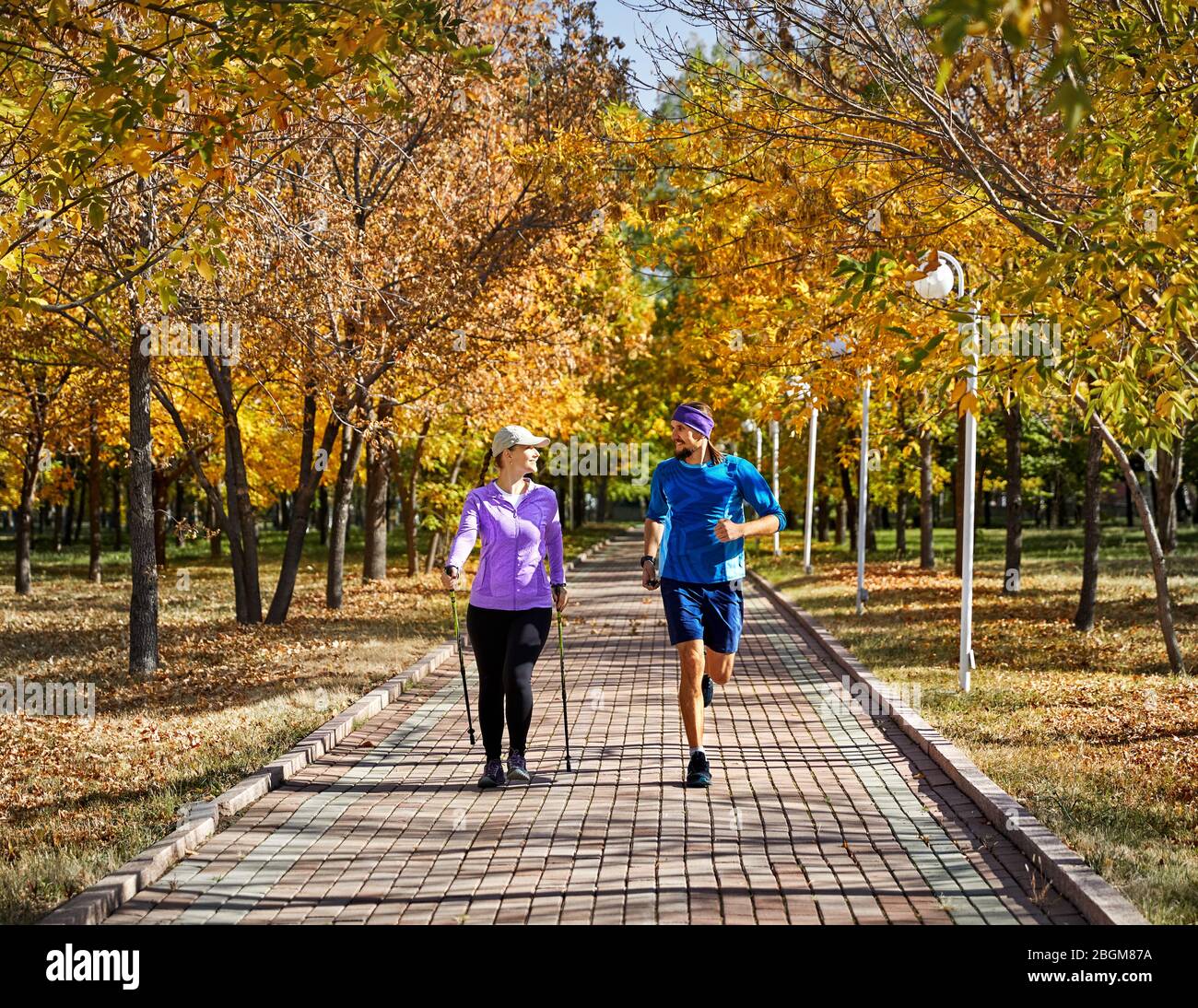 Junges Paar Training im Herbst Park. Mann und Frau tun ist Joggen Nordic Walking mit Stöcken. Gesundes Leben Konzept. Stockfoto