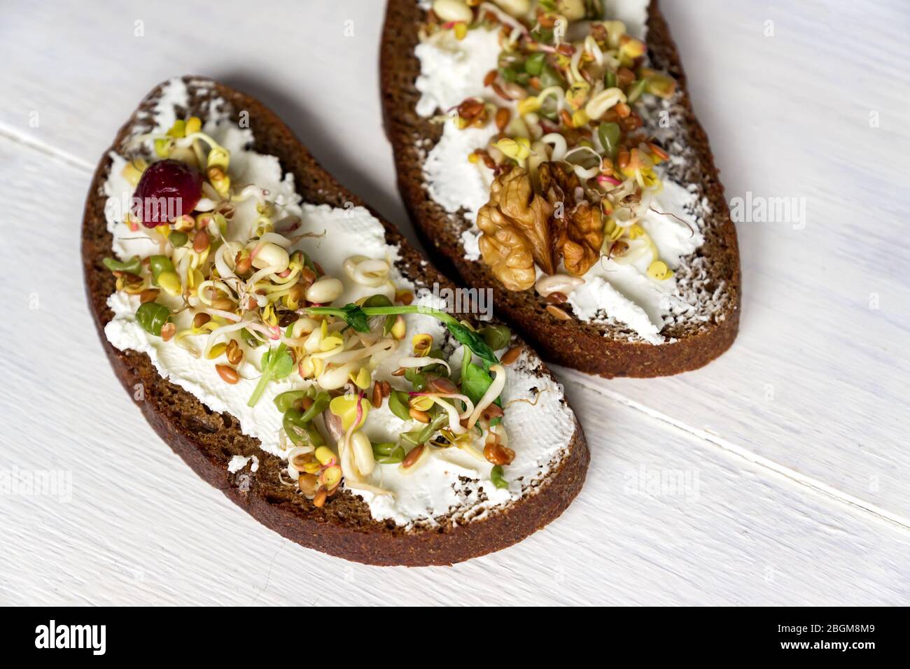 Gesundes makrobiotisches Frühstück. Sandwich mit Frischkäse, Erbsen-Mikrogreens und gekeimten Mungbohnen, Walnuss, Sonnenblume und Flachs auf Holzhintergrund. Stockfoto