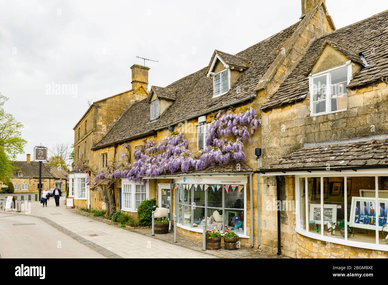 Geschäfte am Straßenrand, lokaler Stil und Glyzinien in Blumen in High Street, Broadway, Worcestershire, ein wunderschönes Dorf in den Cotswolds, Südwestengland Stockfoto