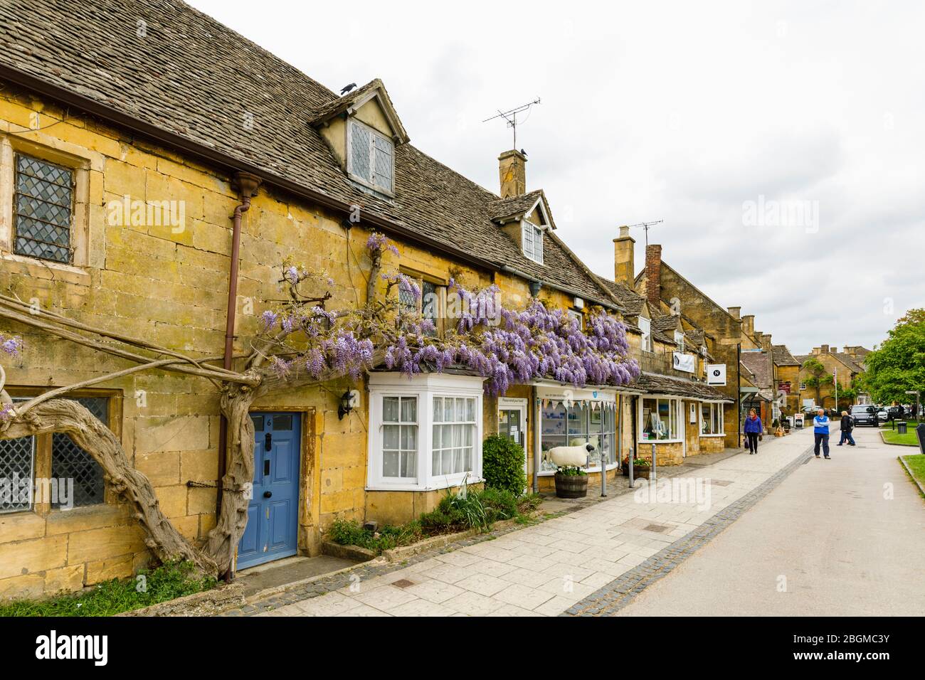 Geschäfte am Straßenrand, lokaler Stil und Glyzinien in Blumen in High Street, Broadway, Worcestershire, ein wunderschönes Dorf in den Cotswolds, Südwestengland Stockfoto