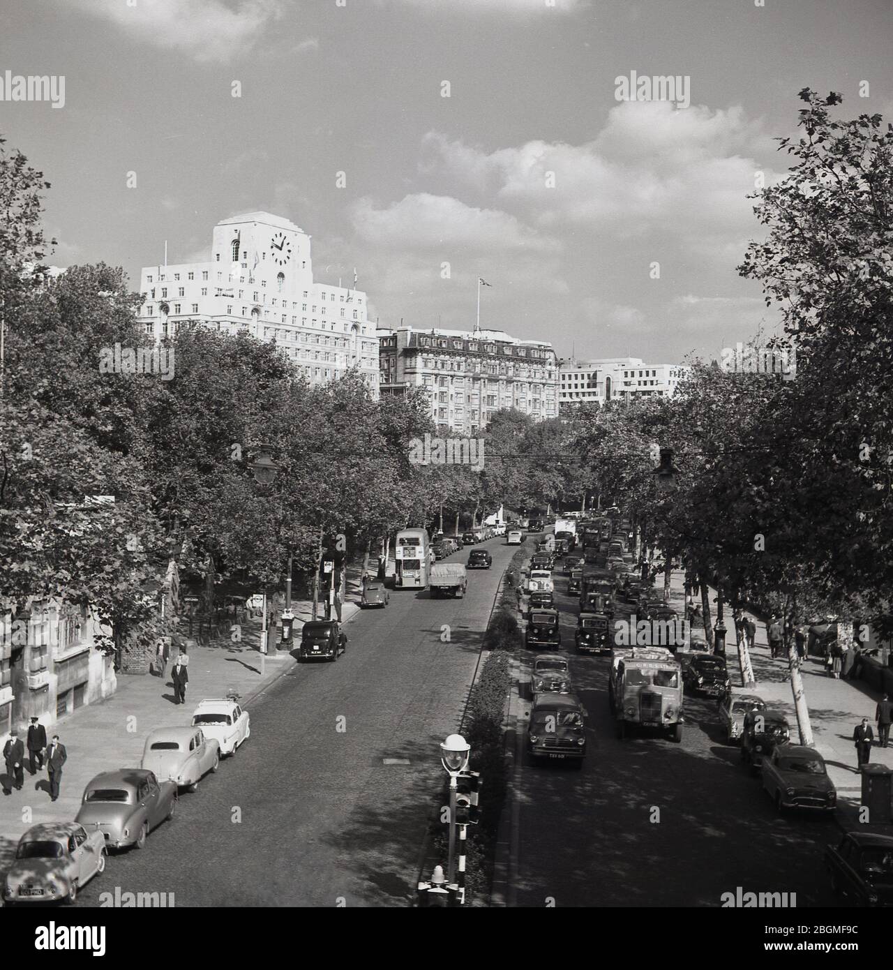 1950er Jahre, historisch, ein Blick entlang der Victoria Embankment in Westminster, London, England, Großbritannien, zeigt die Fahrzeuge der Ära und in der Entfernung Shell Mex Haus mit seiner externen Uhr. Die von Bäumen gesäumte Straße liegt am Nordufer der Themse und verläuft vom Palace of Westminster zur Blackfriars Bridge in London. Stockfoto