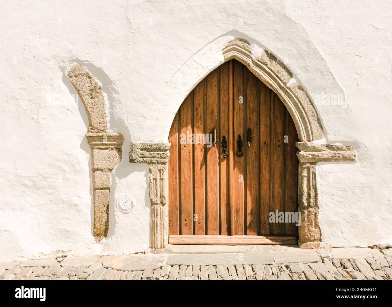 Schöne mittelalterliche Tür in Form eines Bogens, umgeben von den traditionellen weißen Wänden des malerischen Dorfes Monsaraz, Portugal Stockfoto