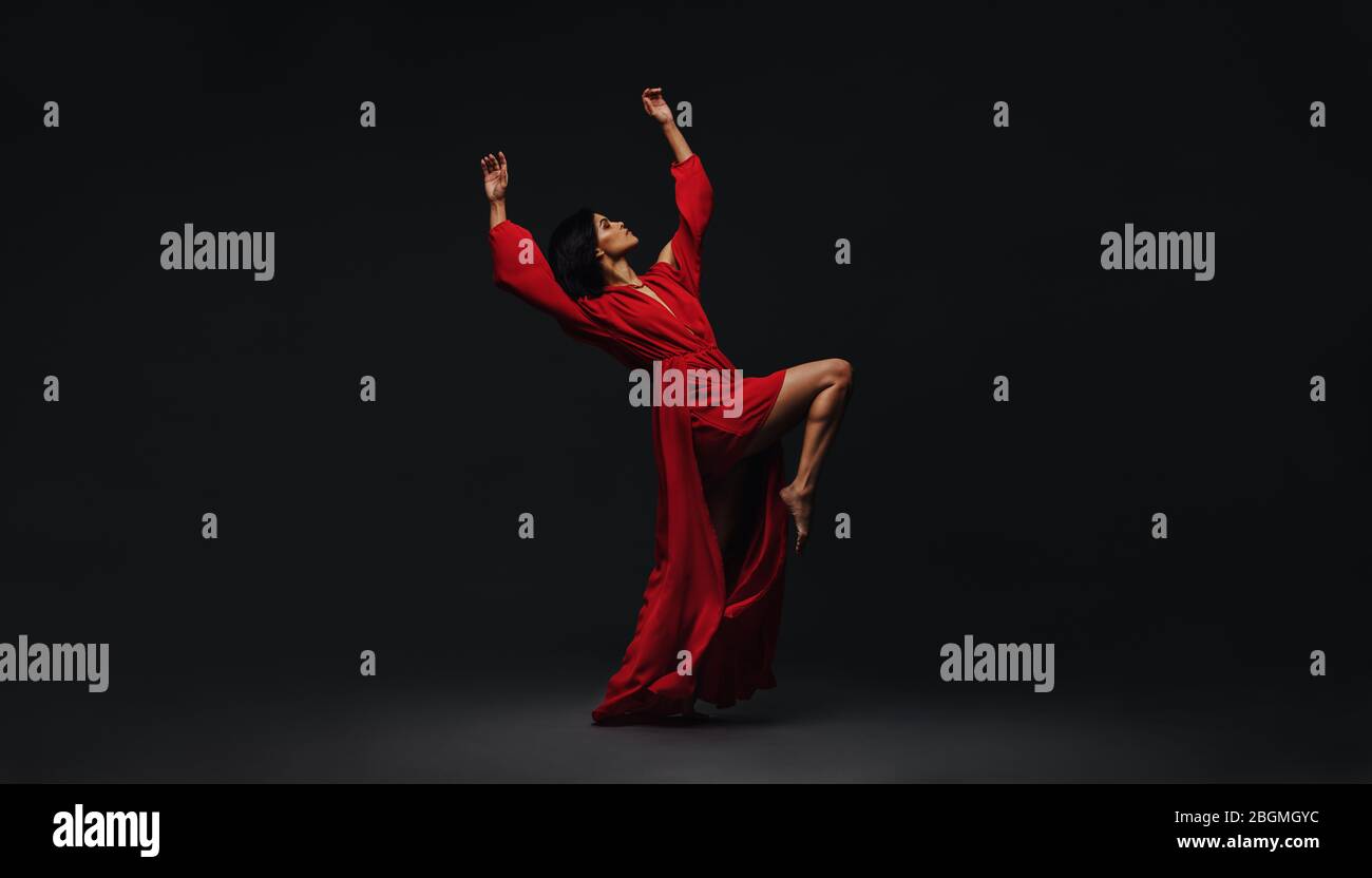 In voller Länge tanzt eine junge Frau im Studio. Zeitgenössische Tänzerin in rotem Kleid, die auf schwarzem Hintergrund aufführt. Stockfoto
