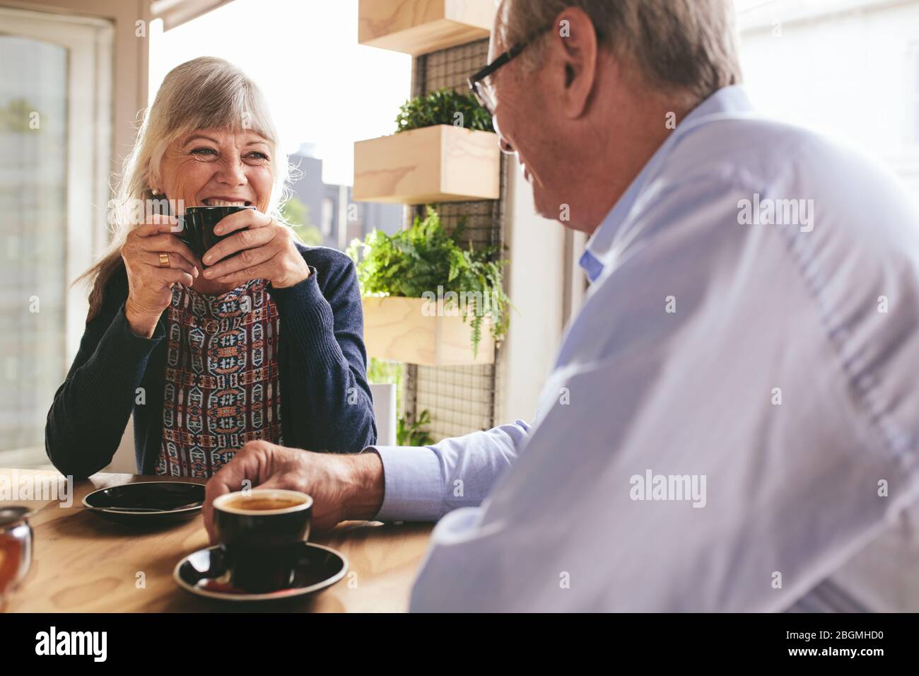 Älteres Paar sitzt am Tisch und trinkt Kaffee im Café. Fröhliches älteres Paar, das sich unterhält und eine Tasse Kaffee im Café genießt. Stockfoto