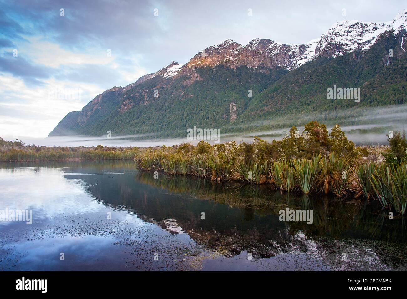 Sunrise, Spiegel Seen im Fjordland National Park, Neuseeland. Sonnenlicht fällt auf verschneiten Gipfeln, in ruhigen, klaren Wasser wider. Stockfoto