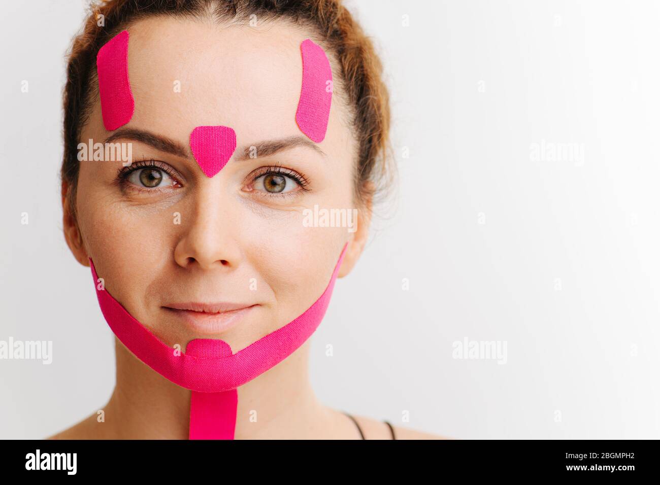 WPorträt einer jungen Frau mit rosa Anti-Falten-Klebeband auf ihrem Gesicht über weiß Stockfoto