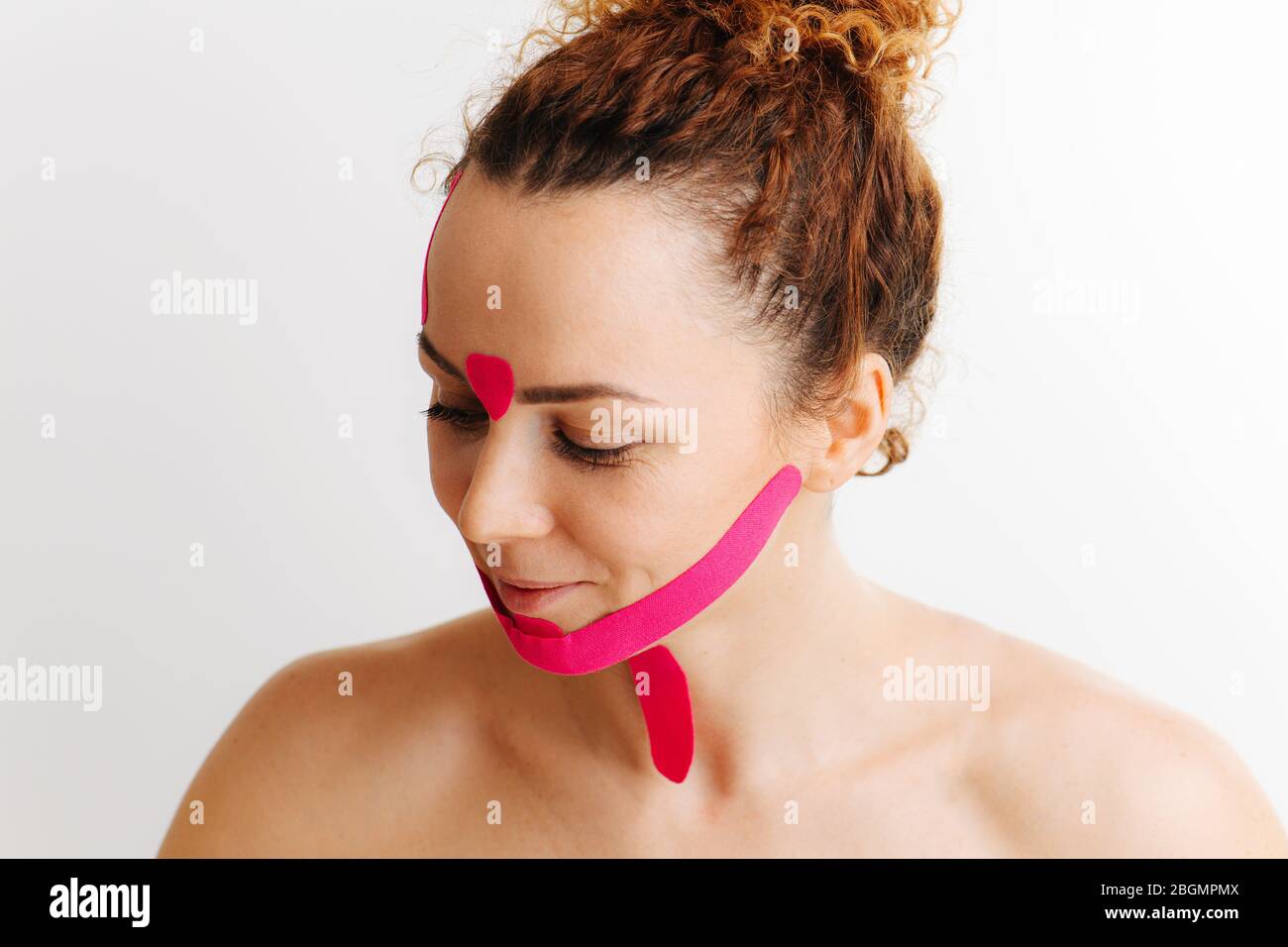 Amüsiert kichernd schüchterne Frau mit rosa Anti-Falten-Band auf ihrem Gesicht über weiß Stockfoto
